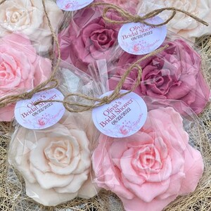 Puede incluir: Un conjunto de seis favores para una despedida de soltera, cada uno con una rosa de jab&oacute;n hecha a mano en una bolsa de pl&aacute;stico transparente atada con una cuerda. Las rosas de jab&oacute;n son en tonos de rosa y blanco, y cada bolsa tiene una etiqueta redonda con el texto "Olivia's Bridal Shower 08/22/2022".