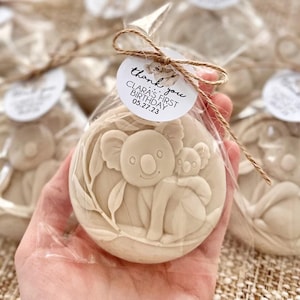 May include: A beige, round cookie with a koala bear design, packaged in a clear cellophane bag and tied with twine. The cookie features a koala and baby koala surrounded by leaves. A small white tag reads "thank you" and "Clara's First Birthday 05.27.23".