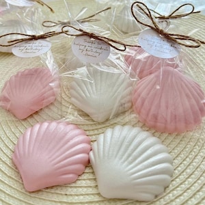 May include: Pink and white seashell shaped favors with a thank you message for helping celebrate a birthday. The message reads "Thanks for helping me celebrate my birthday! -Amelia".