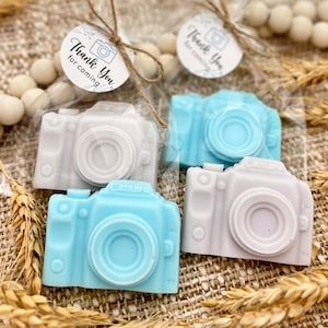 May include: Four small camera-shaped soaps, two in light blue and two in light gray, with the word "Camera" printed on them. The soaps are packaged in clear cellophane bags with twine and a small tag that says "Thank You for coming".