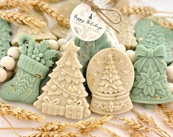 May include: A collection of sage green and cream-colored holiday-themed wax melts shaped like stockings, Christmas trees, snow globes, and bells. A clear plastic bag contains additional wax pieces with a tag reading Happy Holidays FROM THE WALKERS 2026.
