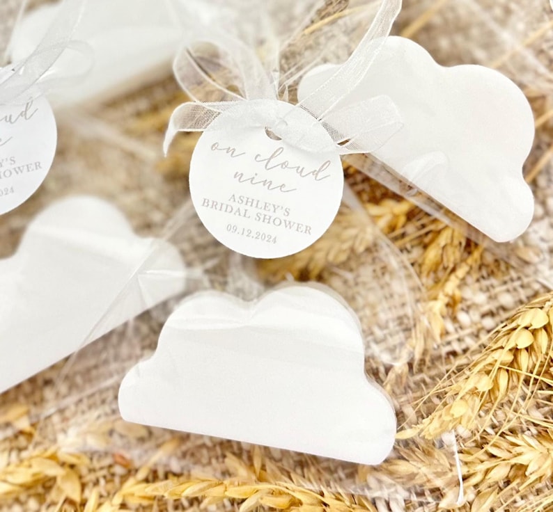May include: White cloud-shaped soap favors with a round tag that reads "on cloud nine" and "Ashley's Bridal Shower 09.12.2024".