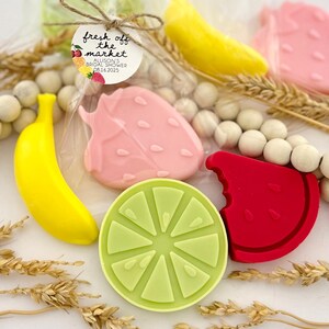 May include: Assortment of fruit-shaped soaps, including a banana, strawberry, watermelon, and lime. The soaps are packaged in clear cellophane bags with a tag that reads "fresh off the market Allison's Bridal Shower 08.16.2023".