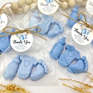 Może przedstawiać: Niebieskie torebki na prezenty dla dziecka z podziękowaniem z napisem "Thank You Alicia's Baby Shower 09.15.2025". Torebki zawierają niebieskie mydła w kształcie butelki, body i odcisku stopy.