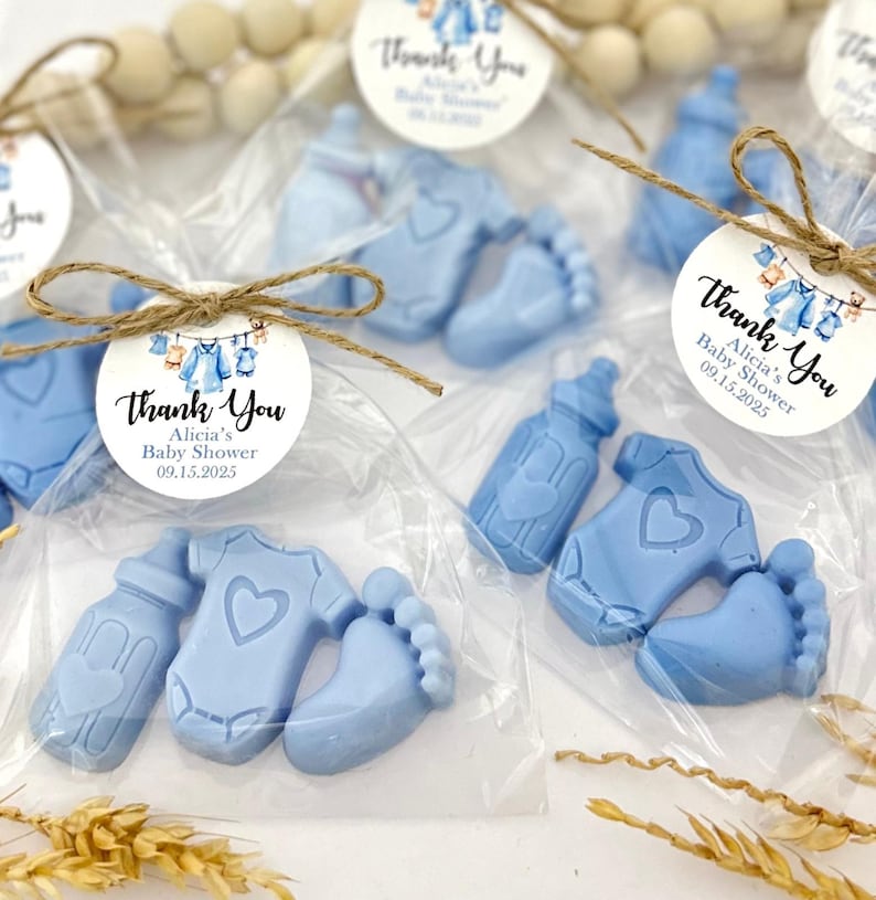 Może przedstawiać: Niebieskie torebki na prezenty dla dziecka z podziękowaniem z napisem "Thank You Alicia's Baby Shower 09.15.2025". Torebki zawierają niebieskie mydła w kształcie butelki, body i odcisku stopy.