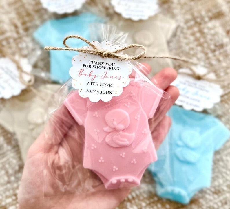 Puede incluir: Jabones en forma de mono de beb&eacute; rosa y azul con purpurina dorada y una etiqueta de agradecimiento que dice "Gracias por celebrar el nacimiento de Baby Jones con amor - Amy & John".