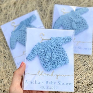 May include: Blue crocheted baby sweater on a hanger with a thank you card that says "Amelia's Baby Shower 09.18.2022"