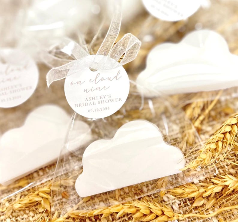 May include: White cloud-shaped favors with a round tag that reads "on cloud nine Ashley's Bridal Shower 09.12.2024".