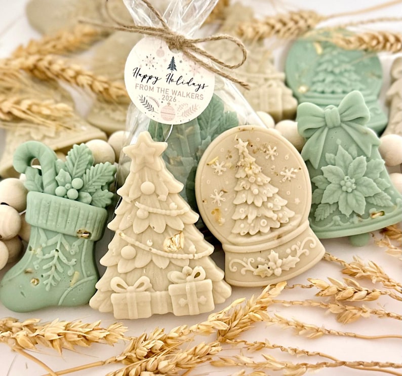 May include: A collection of holiday-themed wax melts in shapes of a stocking, a Christmas tree, a snow globe, and a bell. The items are colored in sage green and cream, with a clear plastic bag tied with twine and a tag reading Happy Holidays FROM THE WALKERS 2026.