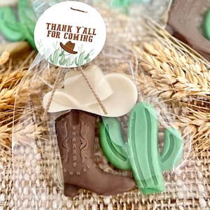 May include: A clear plastic bag filled with a brown cowboy boot, a white cowboy hat, and a green cactus. The bag has a tag attached that says "Thank Y'all For Coming".