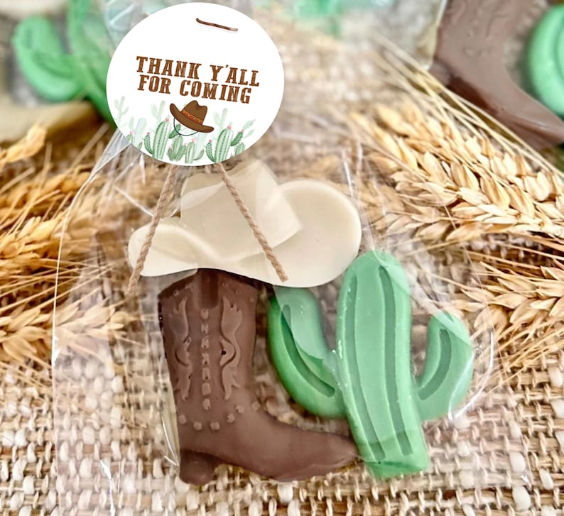 May include: A clear plastic bag filled with a brown cowboy boot, a white cowboy hat, and a green cactus. The bag has a tag attached that says "Thank Y'all For Coming".