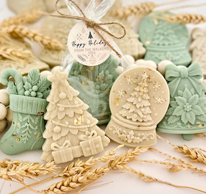 May include: A collection of holiday-themed wax melts in sage green and cream colors, featuring shapes of a Christmas tree, a stocking, a bell, and a snow globe. A clear plastic bag contains a wax melt with a tag reading Happy Holidays FROM THE WALKERS 2026.