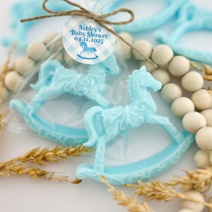 Może przedstawiać: Dwa niebieskie upominki w kształcie konika na biegunach z białą etykietą z napisem "Baby Shower Ashley 04.12.2025" i wzorem w niebiesko-białą kratkę.