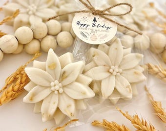 May include: Close-up of white, flower-shaped soaps with a light brown center. The soaps are packaged in clear cellophane bags and tied with twine. A small tag reads "Happy Holidays From The Walkers 2025".