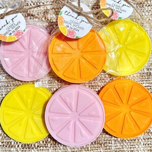 May include: Six round, citrus-shaped soaps in pink, yellow, and orange. The soaps are wrapped in clear plastic bags with thank you tags that say "Olivia's Bridal Shower" and the date.