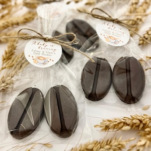 May include: Several cellophane-wrapped coffee bean-shaped favors tied with twine. Each favor has a circular tag that reads "A baby is brewing" and "Ashley & Mark's Baby Shower" with a coffee cup illustration. The favors are brown.