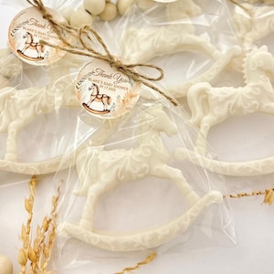Puede incluir: Favores de chocolate blanco en forma de caballo de balanc&iacute;n con una etiqueta de agradecimiento marr&oacute;n y dorada que dice "Gracias Blake's Baby Shower 09.17.2023".