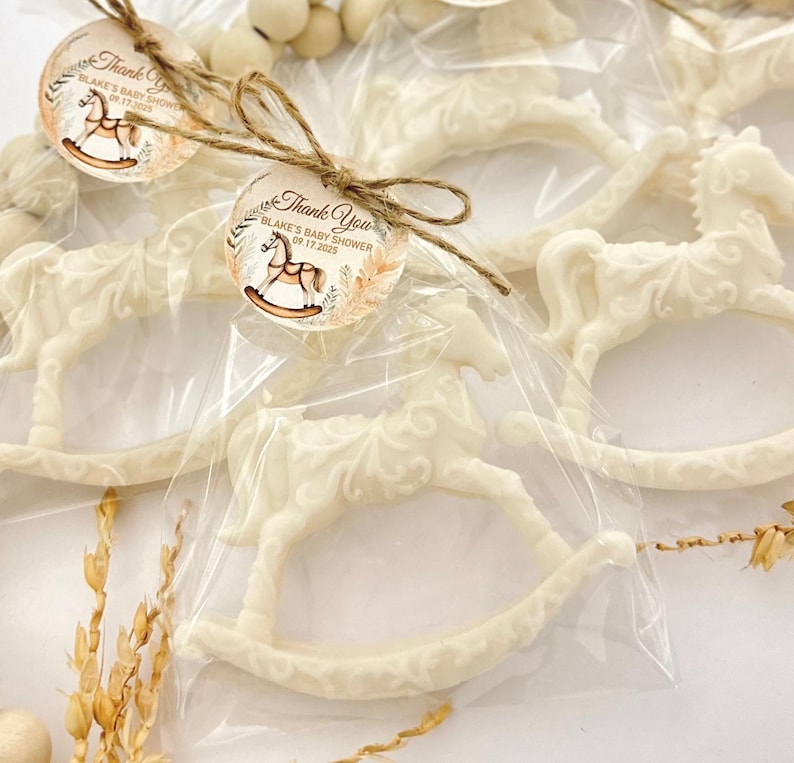 Puede incluir: Favores de chocolate blanco en forma de caballo de balanc&iacute;n con una etiqueta de agradecimiento marr&oacute;n y dorada que dice "Gracias Blake's Baby Shower 09.17.2023".