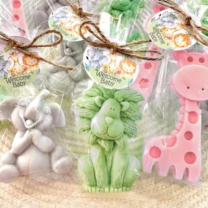 Puede incluir: Surtido de peque&ntilde;os jabones con forma de animales envueltos en bolsas de celof&aacute;n transparentes con un lazo de cuerda marr&oacute;n. Cada jab&oacute;n presenta un animal diferente, incluyendo una jirafa, un le&oacute;n y un elefante. Las bolsas tienen una etiqueta circular con el texto "Welcome Baby" impreso en ellas.