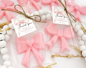 Op de afbeelding: Roze strik-vormige zeepjes met een bedankkaartje met de tekst "Bedankt Kayla's Baby Shower 08/12/24".