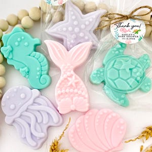 May include: A set of six colorful, handmade soap favors with a nautical theme. The soaps are shaped like a starfish, mermaid tail, seahorse, turtle, jellyfish, and seashell. The soaps are packaged in clear cellophane bags with a thank you tag that reads "Ashley's Baby Shower 10.12.2024".