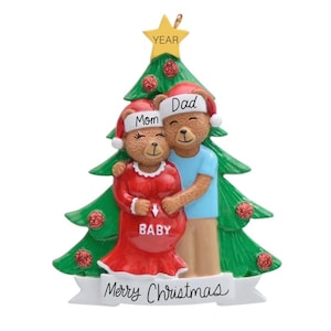 May include: A Christmas ornament featuring a couple of brown teddy bears dressed in red and blue pajamas. The bears are standing in front of a green Christmas tree with red ornaments. The female bear is pregnant and has a sign that says "Baby" on her belly. The ornament has a banner that says "Merry Christmas".