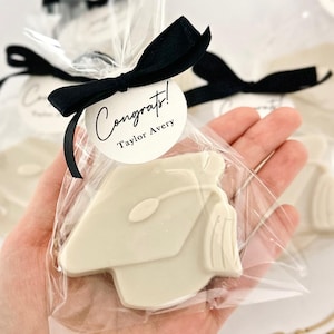 May include: White chocolate graduation cap cookie favor with a black ribbon and a round tag that says "Congrats! Taylor Avery".