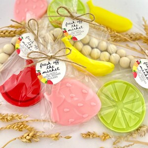 May include: Assortment of fruit-shaped soaps packaged in clear cellophane bags with a small round tag that reads "fresh off the market" and includes the date "08.16.2025". The soaps are shaped like a watermelon slice, strawberry, banana, and lime.