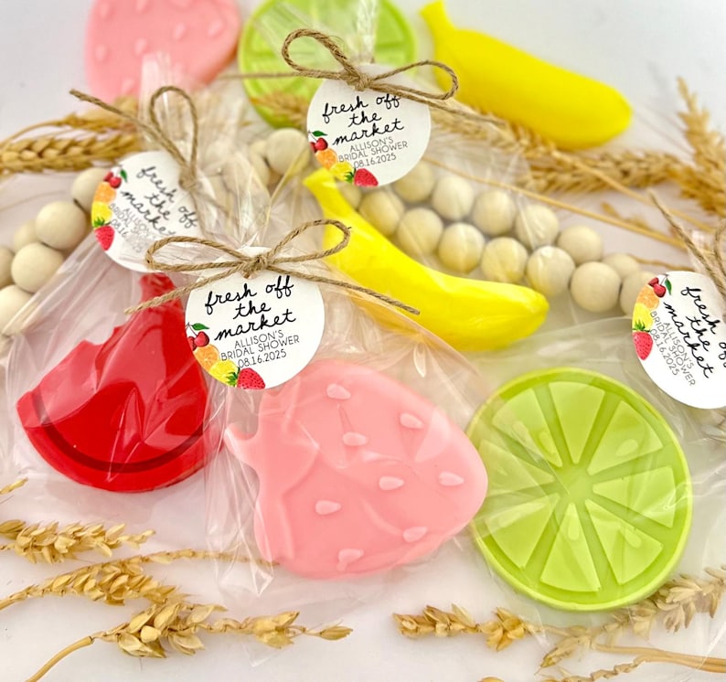 May include: Assortment of fruit-shaped soaps packaged in clear cellophane bags with a small round tag that reads "fresh off the market" and includes the date "08.16.2025". The soaps are shaped like a watermelon slice, strawberry, banana, and lime.
