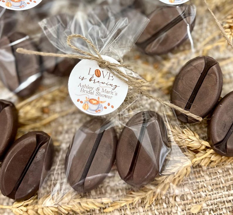 May include: Brown coffee bean shaped favors in clear cellophane bags tied with twine and a round tag that says "Love is brewing Ashley & Mark's Bridal Shower".