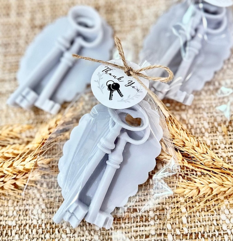 May include: Two silver-colored key-shaped soaps wrapped in clear cellophane with a small tag that says "Thank You" and a small image of keys. The soaps are on a light brown burlap background.