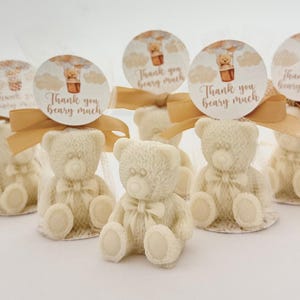 May include: White teddy bear favors with a gold ribbon and a round tag that says "Thank you beary much". The tag has a hot air balloon with a teddy bear in it.