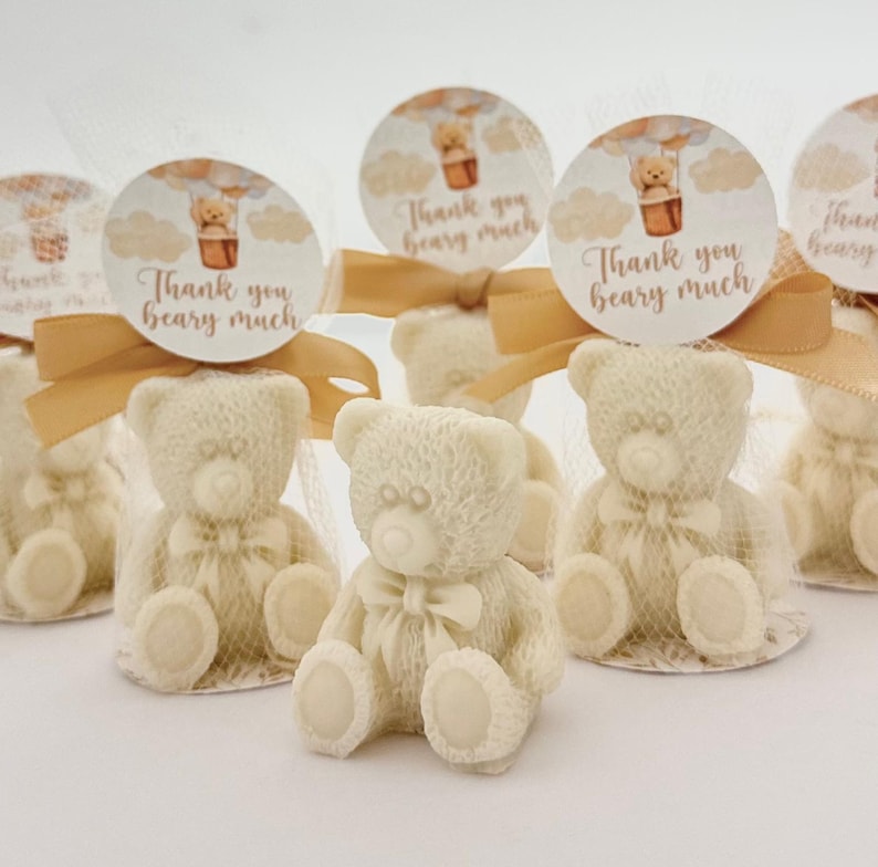 May include: White teddy bear favors with a gold ribbon and a round tag that says "Thank you beary much". The tag has a hot air balloon with a teddy bear in it.