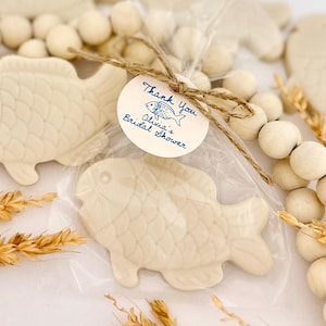 May include: A white ceramic fish-shaped soap dish with a thank you tag that says "Thank You Olivia's Bridal Shower". The tag is tied with twine and has a small blue fish illustration.