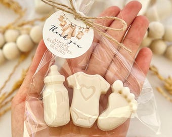 Puede incluir: Una bolsa de celofán transparente atada con hilo, que contiene tres jabones blancos con temática de bebé: un biberón, un body con un corazón y un pie de bebé. Una etiqueta redonda dice "Thank you" y "Alicia's Baby Shower 09.15.2025".