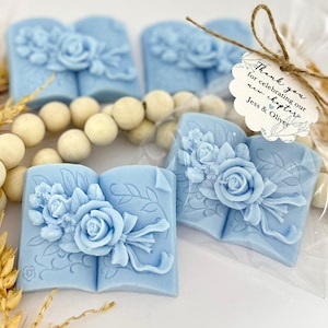 May include: Blue book-shaped soap favors with a floral design and a tag that reads "Thank you for celebrating our new chapter Jess & Oliver".