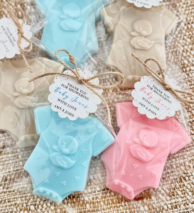 Puede incluir: Gracias por celebrar el nacimiento de Baby Jones con amor - Amy & John. Un conjunto de tres jabones con forma de body de beb&eacute;, uno azul, uno rosa y uno blanco. Cada jab&oacute;n tiene un peque&ntilde;o dise&ntilde;o de pato.