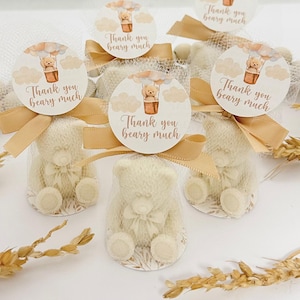 May include: Set of six small white teddy bear favors with a hot air balloon design and the text "Thank you beary much". The favors are wrapped in sheer fabric and tied with a brown ribbon.