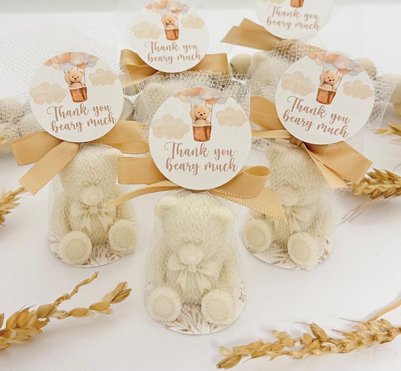 May include: Set of six small white teddy bear favors with a hot air balloon design and the text "Thank you beary much". The favors are wrapped in sheer fabric and tied with a brown ribbon.