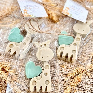 May include: A set of favor bags for a baby shower, each containing a small giraffe-shaped soap and a heart-shaped soap. The bags are tied with twine and have a small tag that says "Thank you for celebrating with us! Baby [Name] 03.17.2024".
