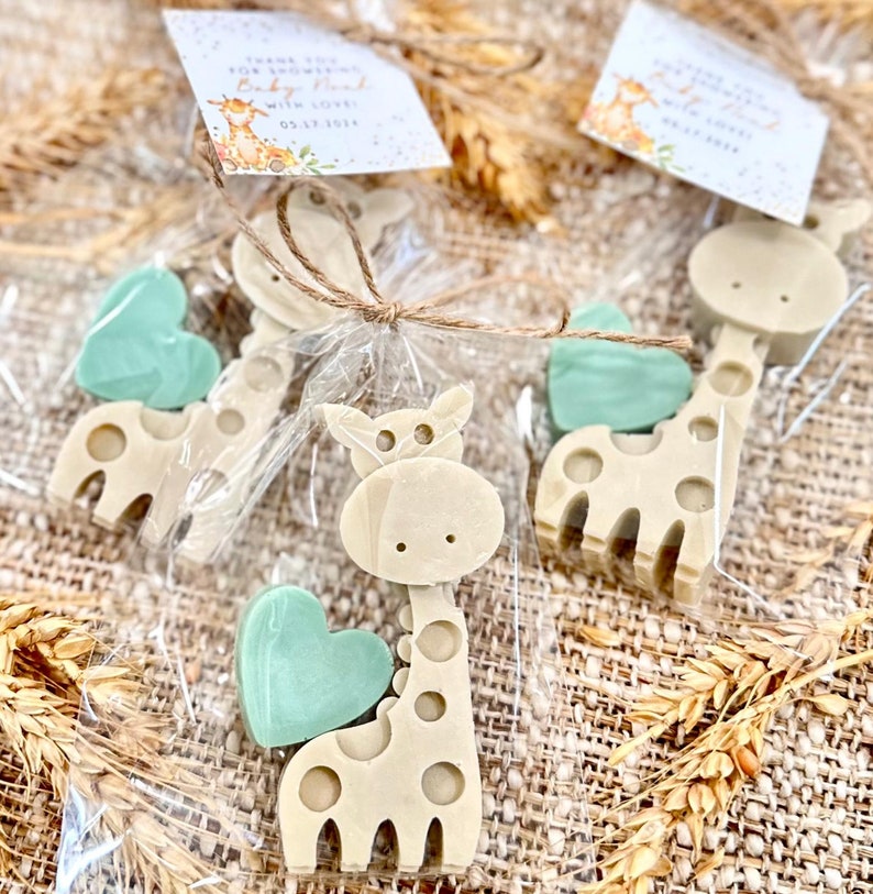 May include: A set of favor bags for a baby shower, each containing a small giraffe-shaped soap and a heart-shaped soap. The bags are tied with twine and have a small tag that says "Thank you for celebrating with us! Baby [Name] 03.17.2024".