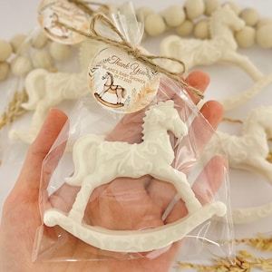 Puede incluir: Un favor de caballo de balanc&iacute;n blanco en una bolsa de celof&aacute;n transparente con un lazo de cuerda marr&oacute;n y una etiqueta de agradecimiento que dice "Gracias Blake's Baby Shower 09.17.2023"