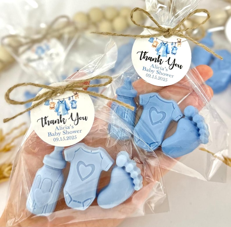 Może przedstawiać: Niebieskie torebki na prezenty z okazji baby shower z etykietą z podziękowaniem, na kt&oacute;rej widnieje napis "Dziękujemy Alicia's Baby Shower 09.15.2025". Torebki zawierają niebieskie mydło w kształcie butelki, body i stopy.