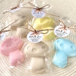 May include: Mushroom shaped soaps in pink, beige, yellow and blue, wrapped in cellophane bags with a brown twine bow. Each bag has a round white tag with the text "thank you OCEAN'S 2ND BIRTHDAY 03.08.2022" printed in black.