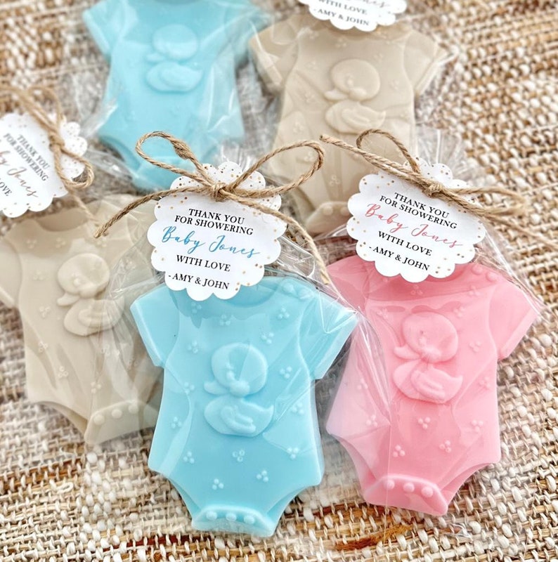 Puede incluir: Gracias por celebrar el nacimiento de Baby Jones con amor, Amy & John. Un conjunto de tres jabones con forma de body de beb&eacute; en azul, rosa y beige, envueltos en bolsas de celof&aacute;n con cuerda y una etiqueta personalizada.