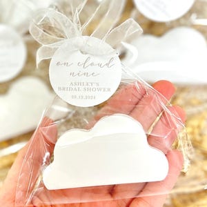 May include: White cloud-shaped favor with a round tag that says "on cloud nine" and "Ashley's Bridal Shower 09.12.2024".