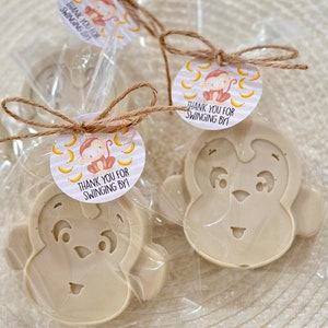 May include: Two small monkey-shaped soaps wrapped in clear cellophane bags with brown twine and a round tag that says "Thank you for swinging by!" with a cartoon monkey and bananas on a striped background.