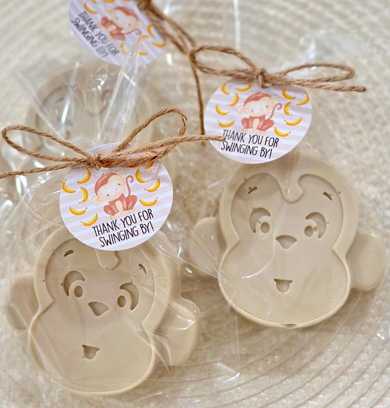 May include: Two small monkey-shaped soaps wrapped in clear cellophane bags with brown twine and a round tag that says "Thank you for swinging by!" with a cartoon monkey and bananas on a striped background.