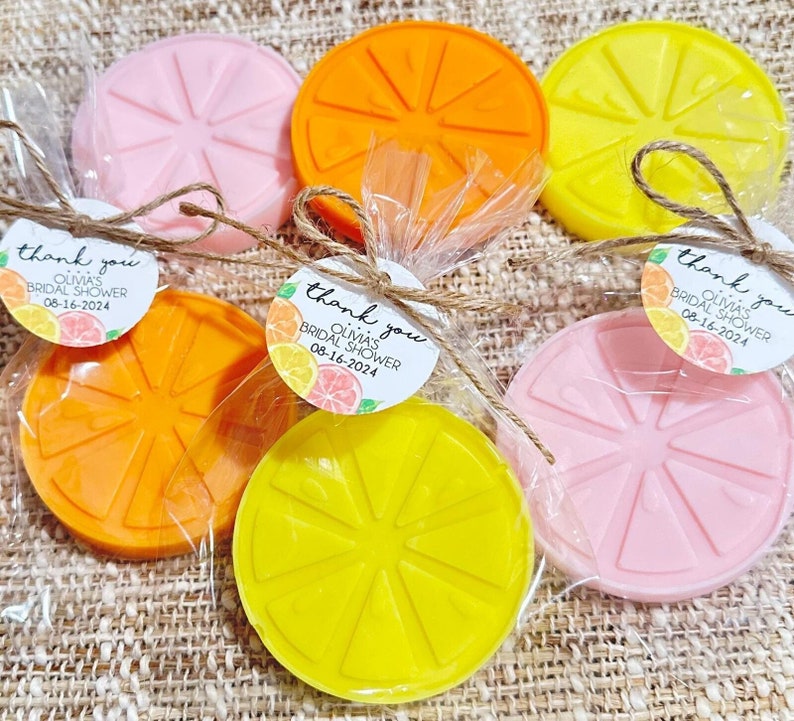 May include: Six small, round, citrus-shaped soaps wrapped in clear cellophane bags with twine and a thank you tag. The soaps are in shades of pink, yellow, and orange. The tags say "Thank you Olivia's Bridal Shower 08-16-2024".
