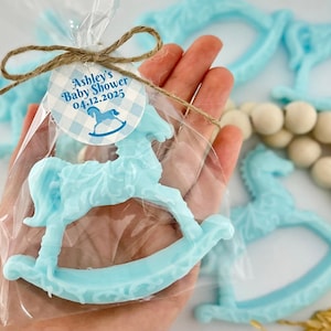 Może przedstawiać: Niebieskie mydło w kształcie konika na biegunach z biało-niebieską kratką z napisem "Ashley's Baby Shower 04.12.2025".